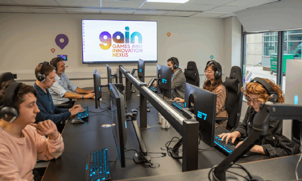 Eight gamers, all wearing headphones, are sat around a table with PC screens.