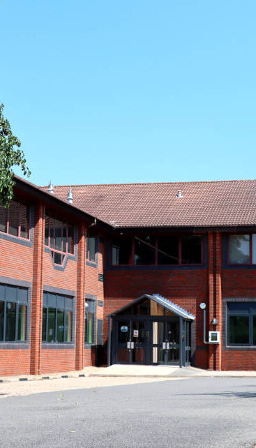 Exterior shot of the front of a two-storey red brick corporate office with an empty car park.